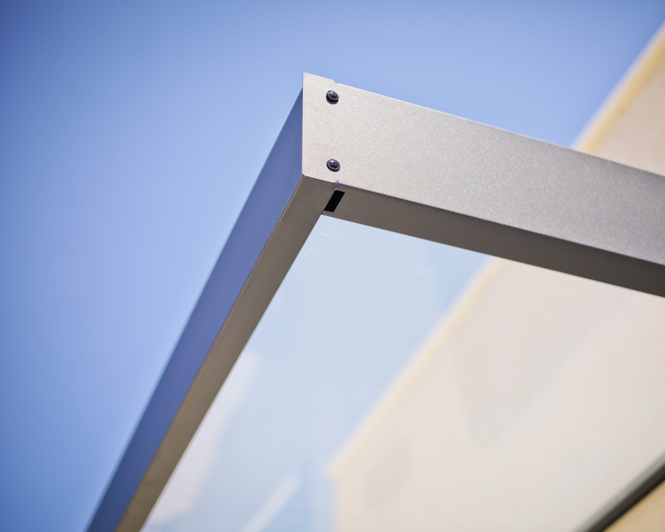 Close-up of the sleek gray aluminum frame of the Sophia 2150 Door Canopy, featuring a minimalist design and built-in gutter system against a clear sky background.